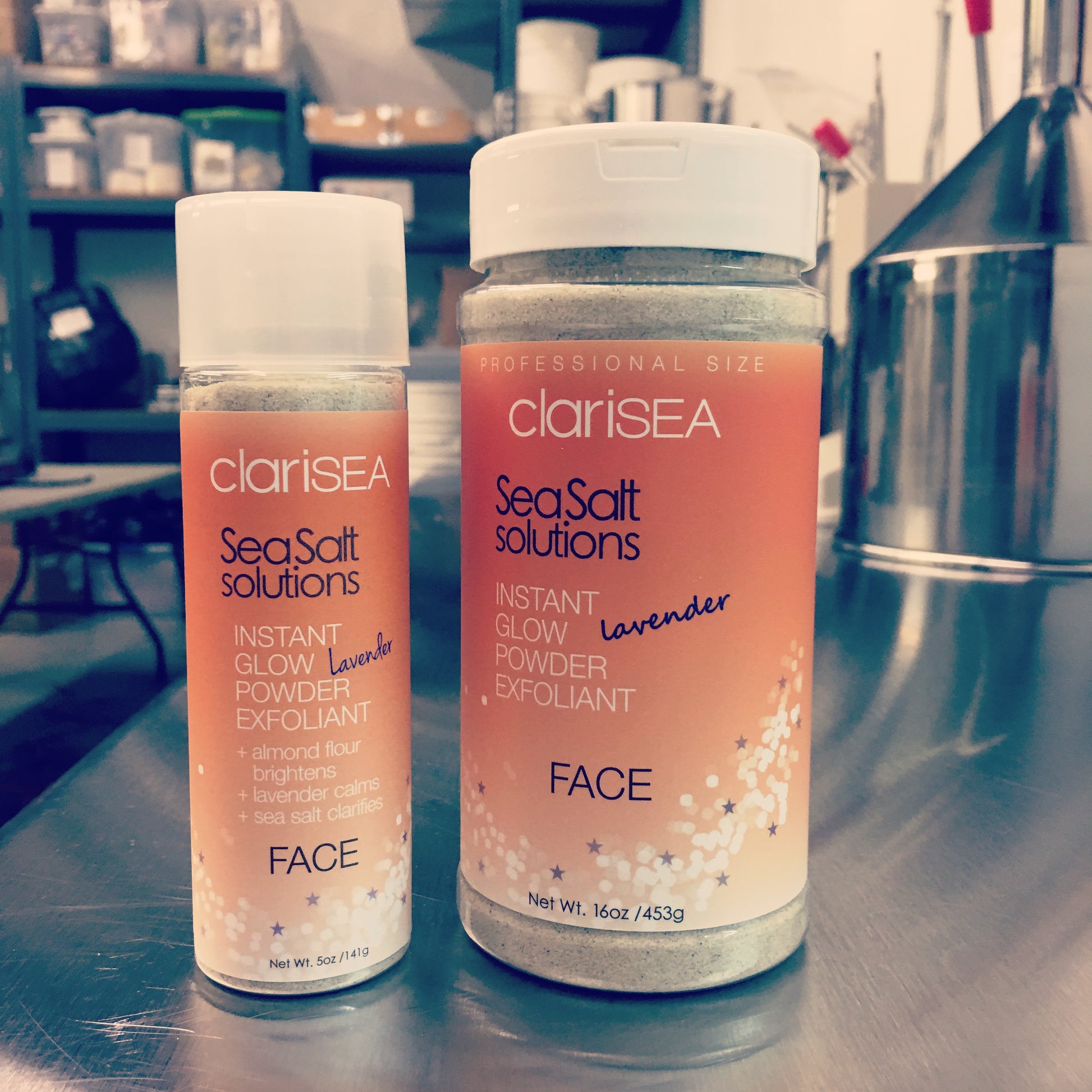 clariSEA Instant Glow Powder Exfoliant 5 oz bottle and 16 oz Pro Size bottle, in studio image on stainless steel work table.